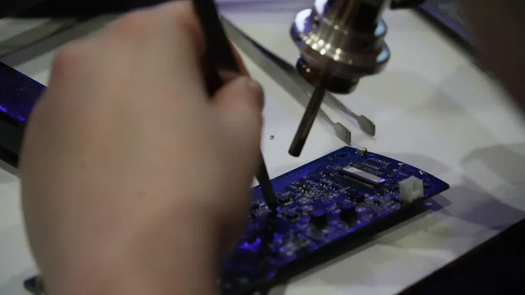 Close-up of a hand using a tool on a blue circuit board during hardware security analysis.