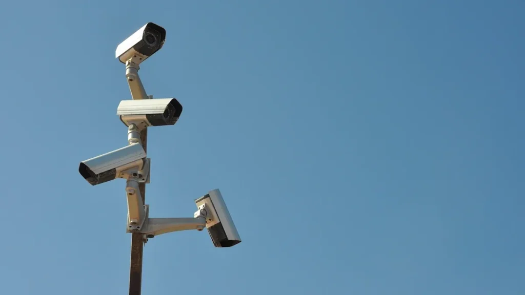 Multiple security cameras on a pole pointing in different directions against a clear blue sky.