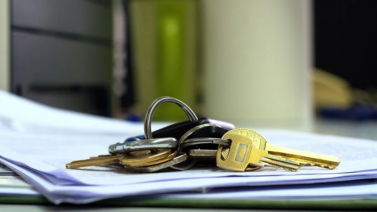 Metallic keys on a keyring lying on a stack of white papers with a blurred office background.