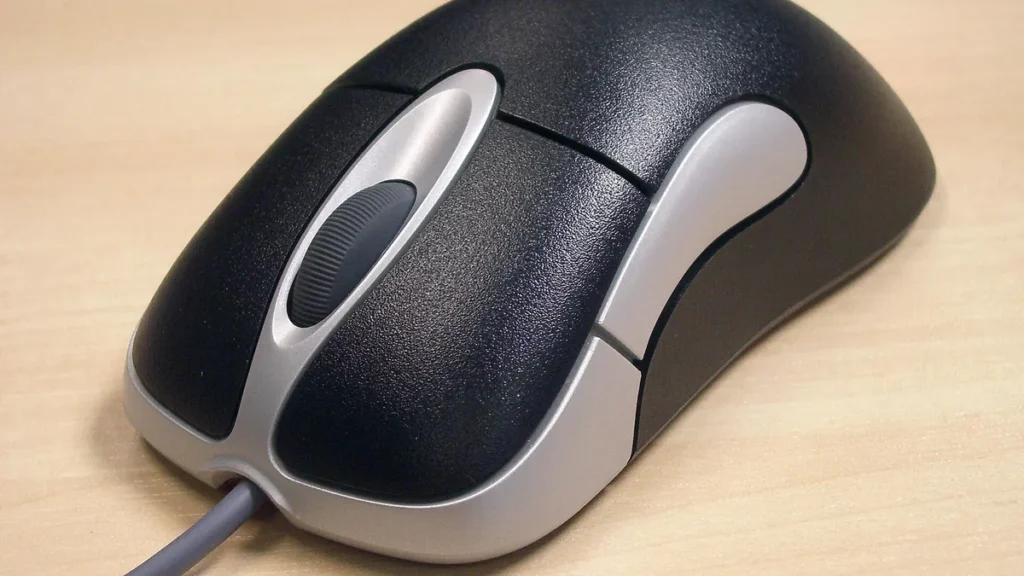 A close-up of a black and silver computer mouse on a light wooden surface.