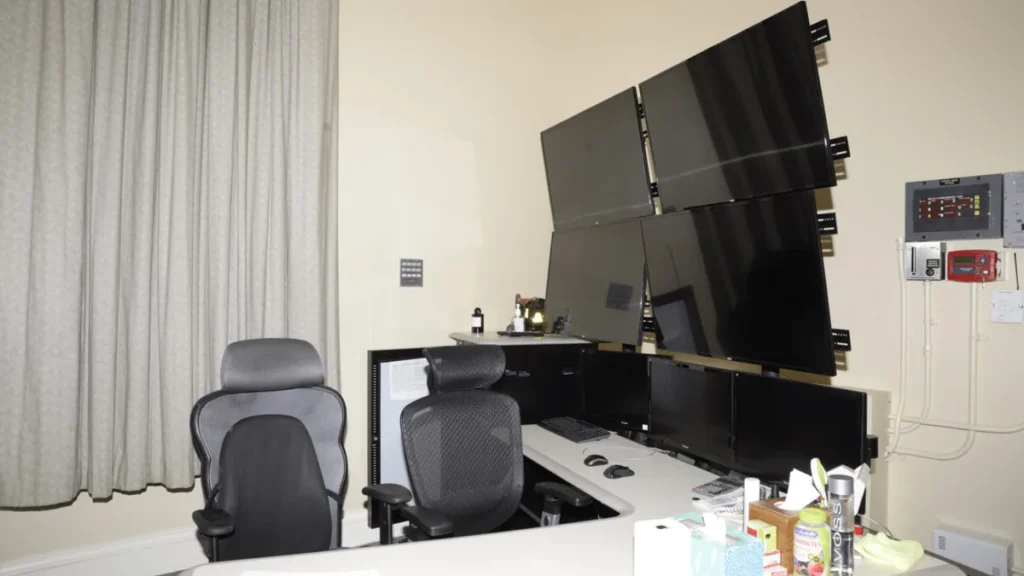 A cybersecurity command center with multiple monitors, office chairs, and control panels on the wall.