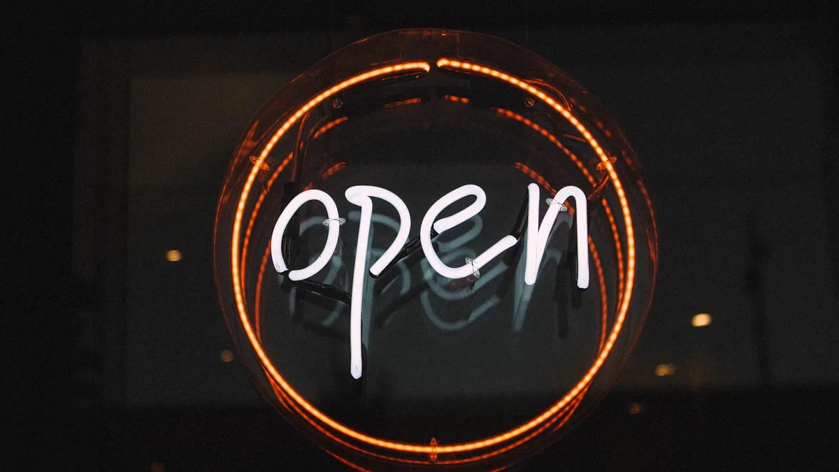 White neon 'open' sign glowing inside an orange circle on a dark, blurry background.