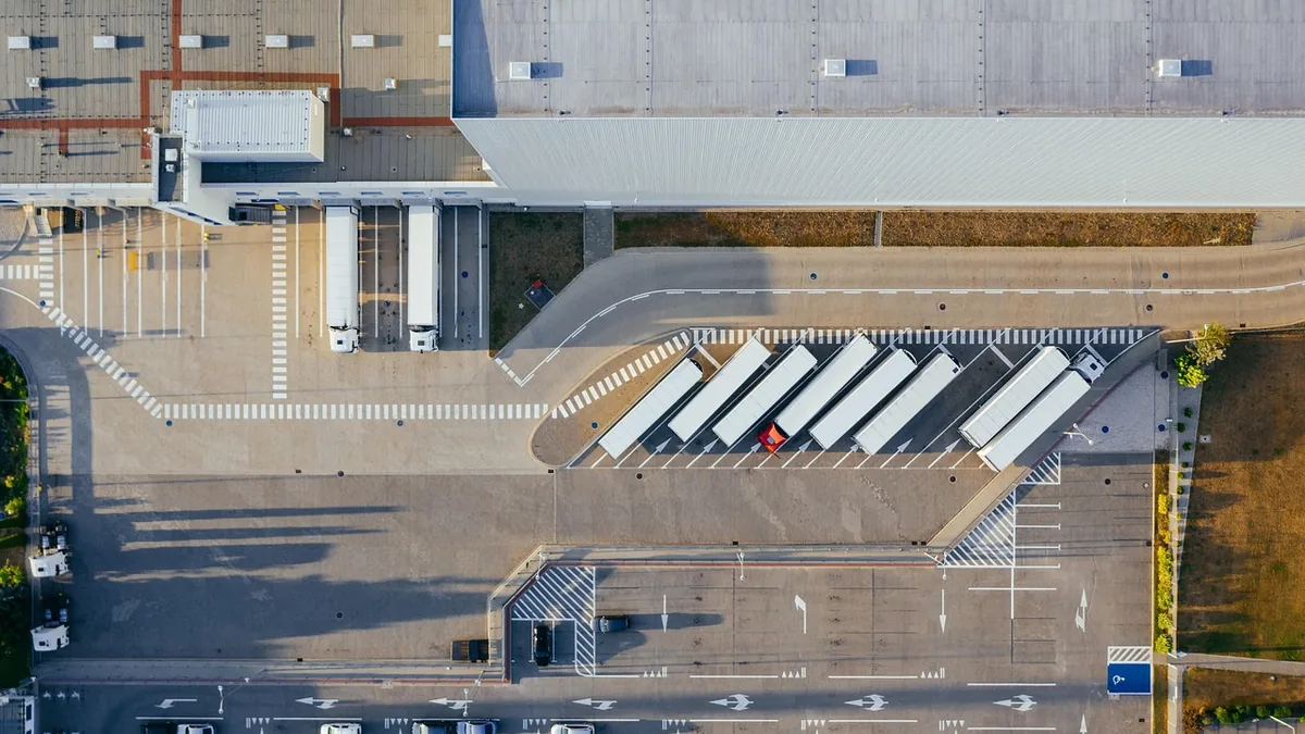 Aerial view of a large logistics warehouse with trucks parked at loading docks and diagonal parking slots.