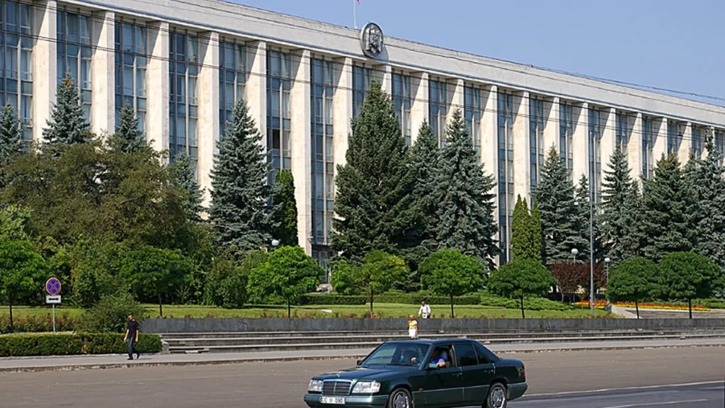 The government building in Chișinău, Moldova, behind a green car on a sunny day.