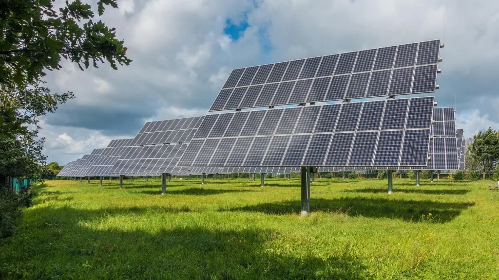 Solar panel array in a green field under a cloudy sky, representing green energy grid assets.