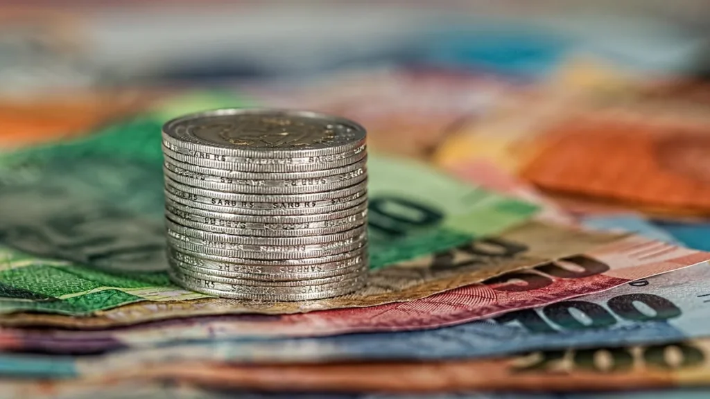 Stack of silver coins on colorful banknotes representing money.