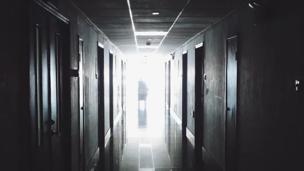 Silhouette of a person at the bright end of a dark hospital hallway.