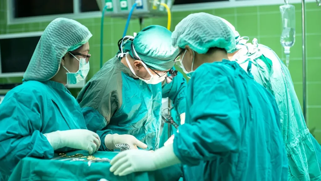 A surgical team in green scrubs performs a medical procedure in an operating room.