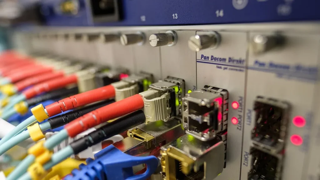 Close-up of colorful fiber optic and network cables plugged into a switch panel with status lights.