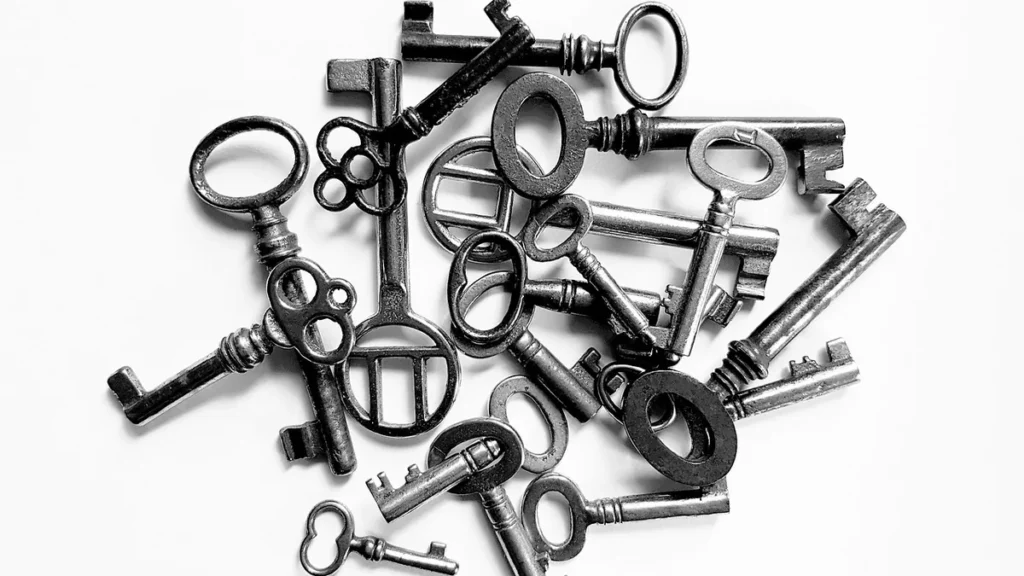 Black and white photo of a pile of old-fashioned metal keys scattered on a white surface.