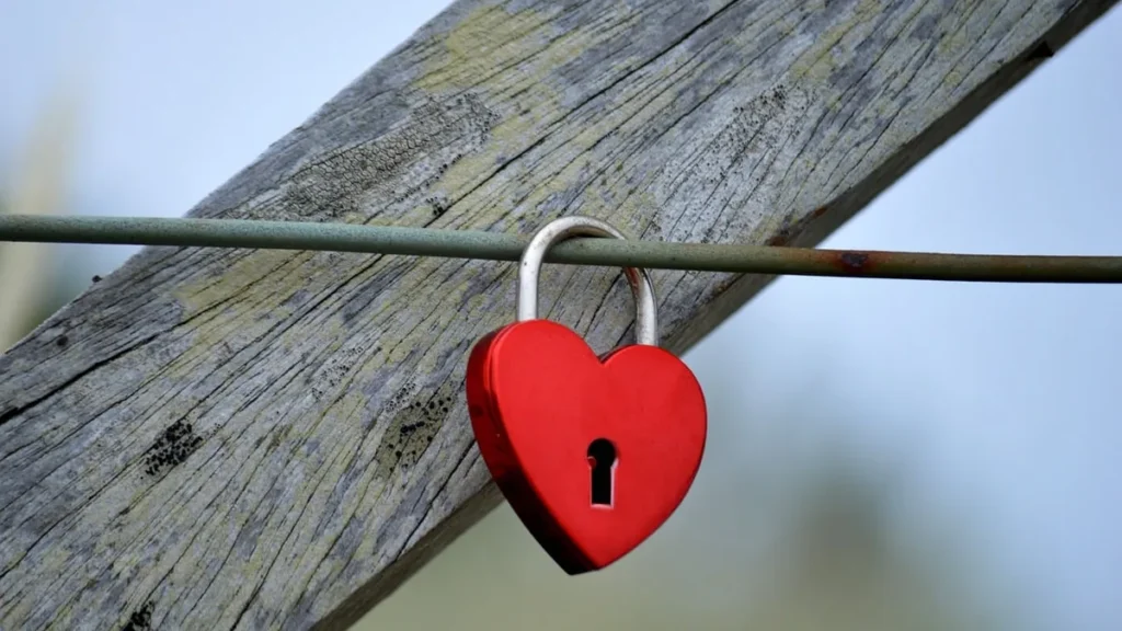 Red heart-shaped padlock hanging on a wire with a wooden beam background, representing privacy and security.