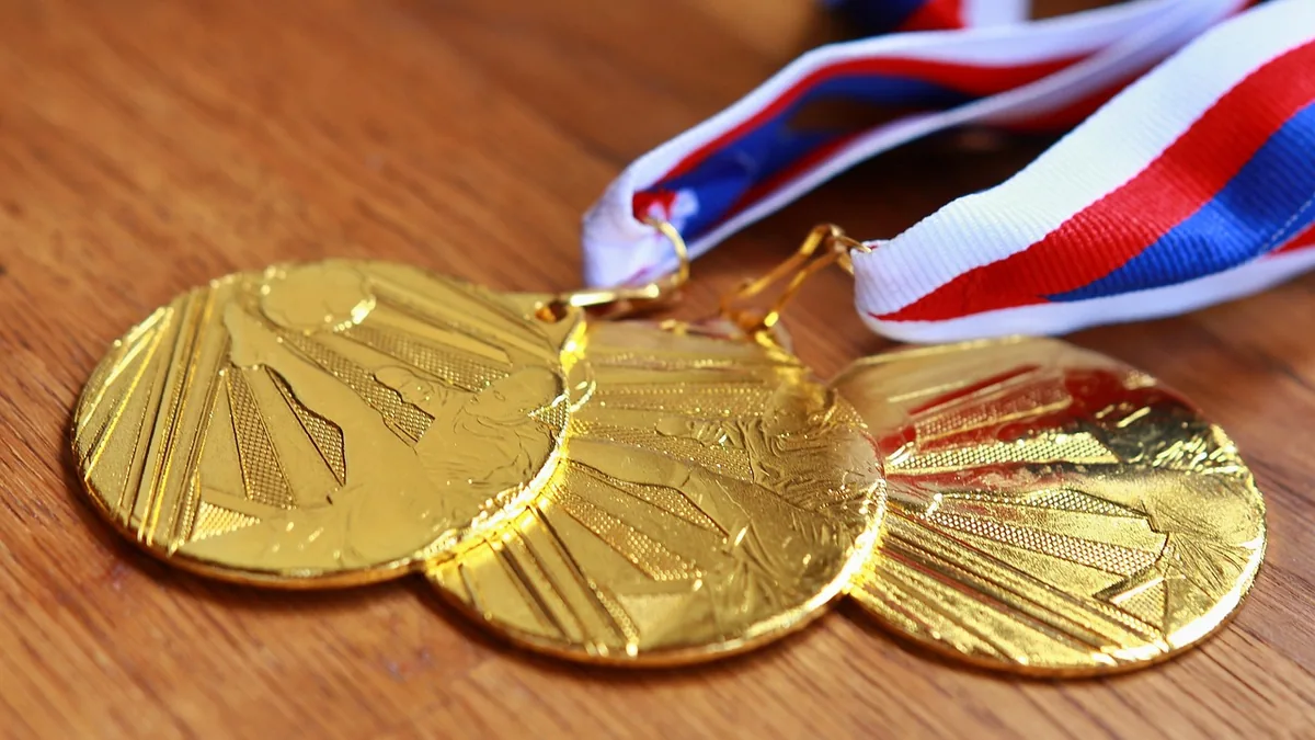 Three shiny gold medals with red, white, and blue ribbons lie on a wooden surface, symbolizing achievement.