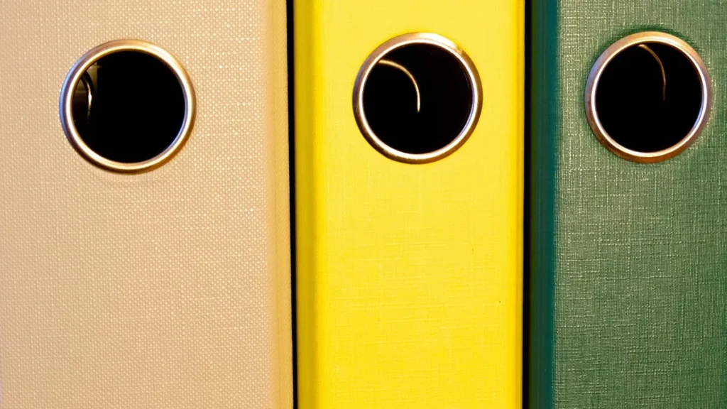 Beige, yellow, and green binders with circular metal holes, symbolizing stored records and files.