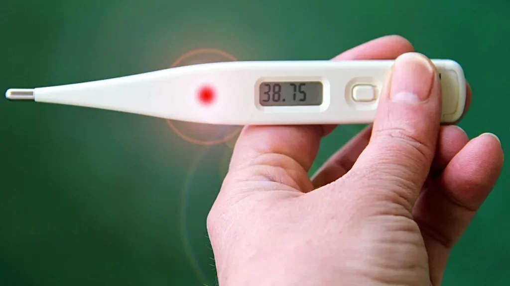A hand holding a white digital thermometer displaying a high temperature reading of 38.75 degrees.