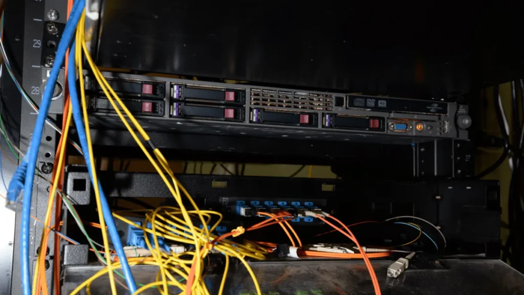 Server rack with tangled yellow, blue, and orange network cables connected to hardware.