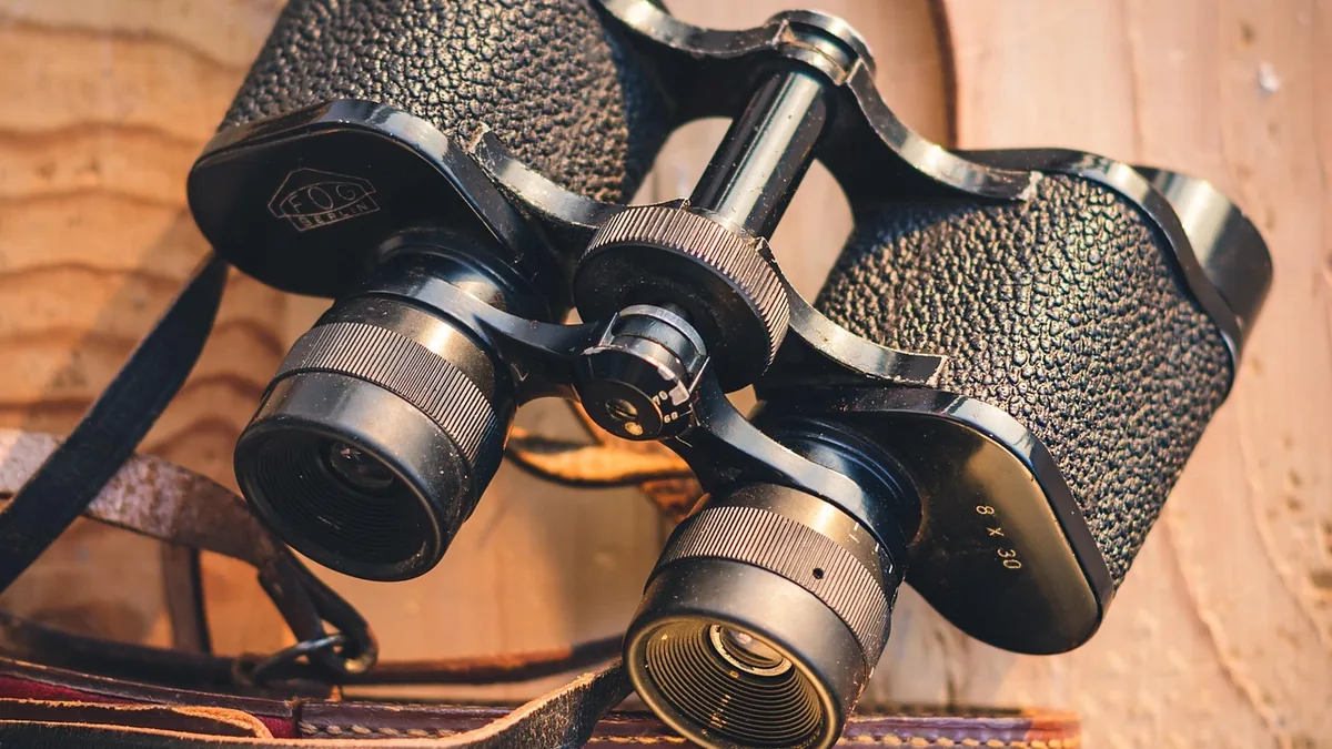 Close-up of black vintage binoculars with textured grip on a wooden surface.