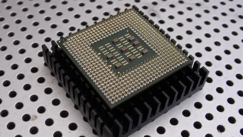 A microprocessor with gold pins resting on a black heatsink on a perforated metal surface.