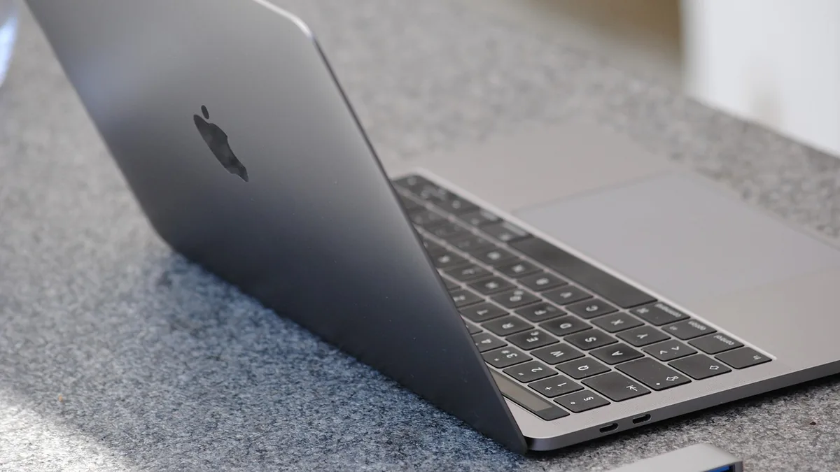 A silver MacBook laptop showing the Apple logo, keyboard, and trackpad on a grey textured surface.