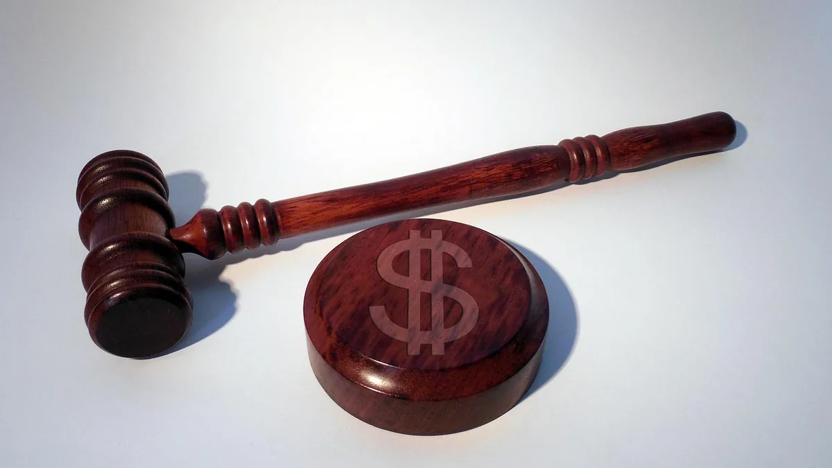 A wooden gavel lying next to a round block engraved with a dollar sign, symbolizing a financial court ruling.