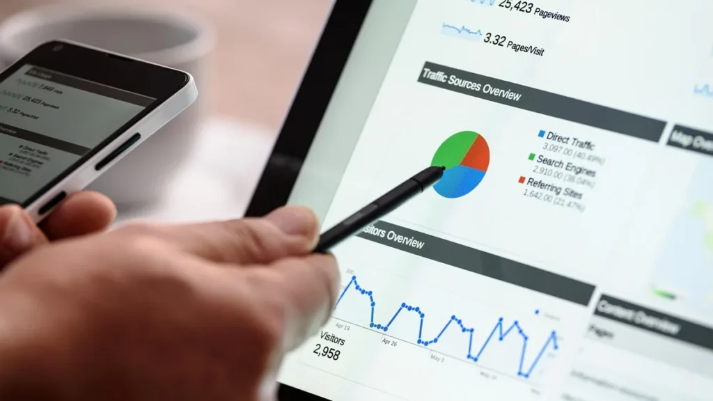 Hand pointing a stylus at web traffic analytics on a tablet screen, showing a pie chart and visitor graphs.