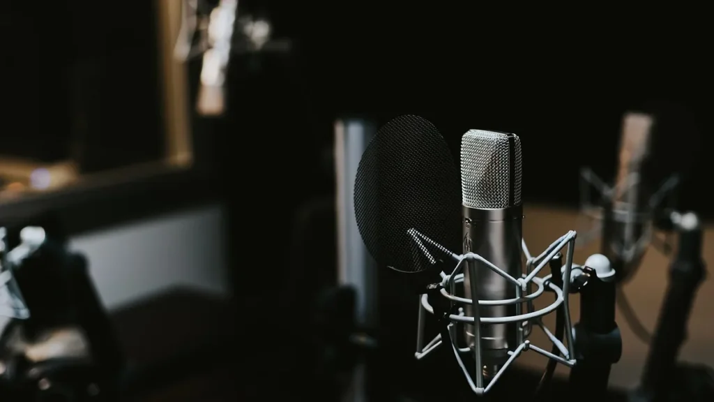 Silver studio condenser microphone with a black pop filter on a shock mount in a dark setting.