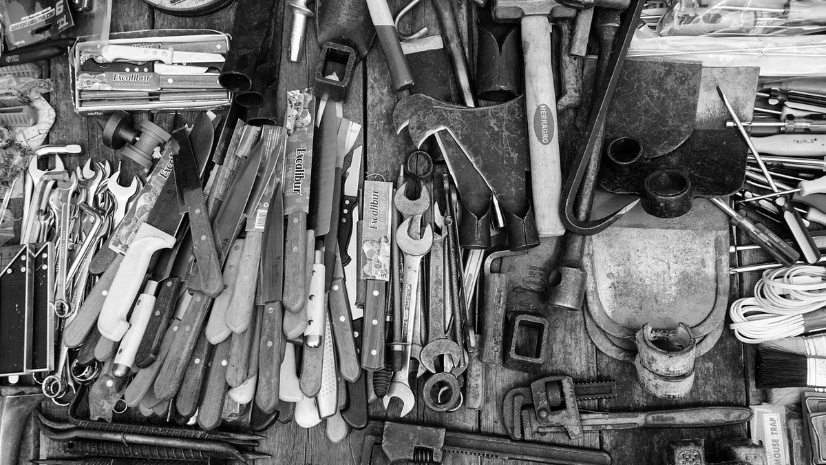Black and white overhead view of a cluttered assortment of hand tools, knives, and wrenches.