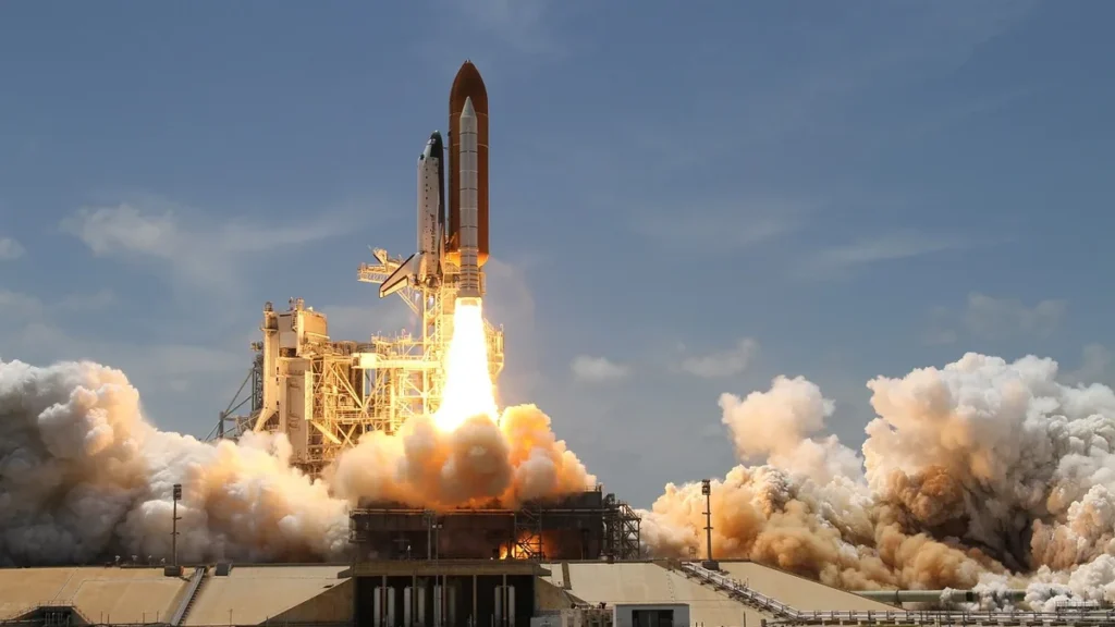 A space shuttle lifts off the launch pad with bright flames and massive clouds of billowing smoke.