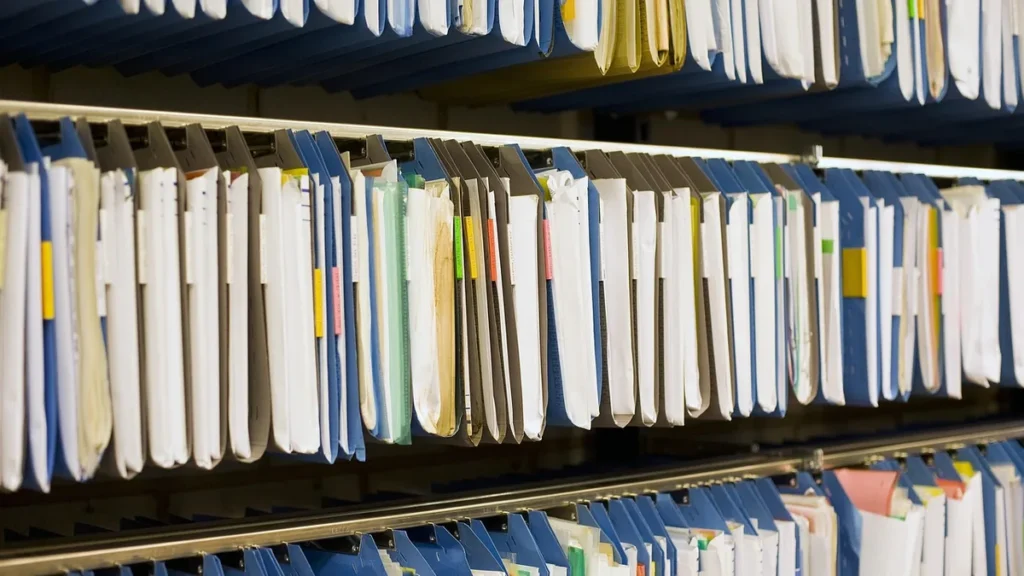 Rows of blue and white hanging file folders on metal shelves, representing archived customer records.