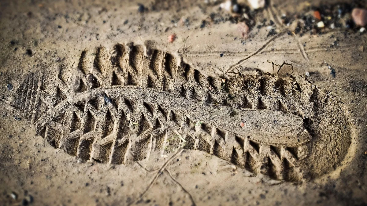 A detailed close-up of a single shoe print deeply impressed in sandy dirt, showing the tread pattern clearly.