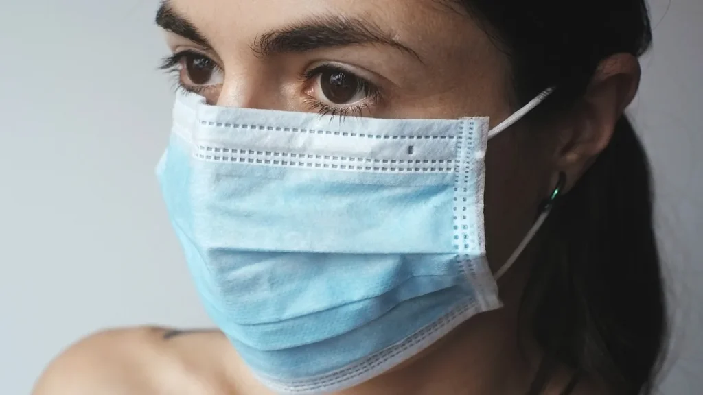 Close-up portrait of a woman wearing a blue surgical mask, looking off-camera.