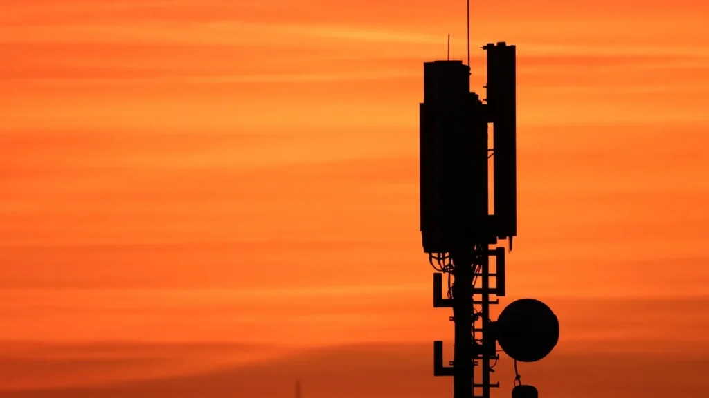 Silhouette of a cellular tower against a vibrant orange sunset sky, representing telecom infrastructure.
