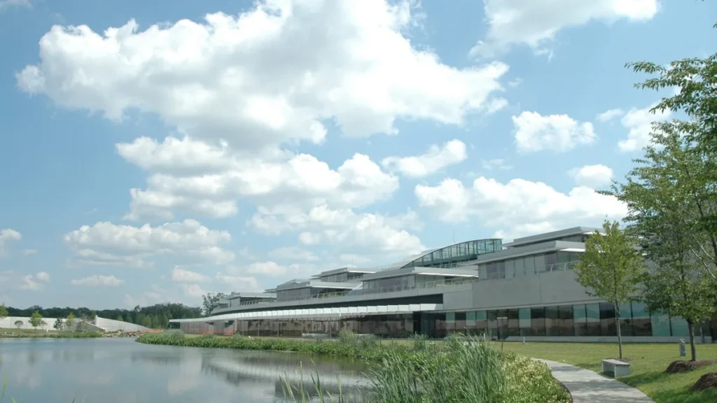 Modern corporate office building next to a pond under a partly cloudy blue sky.