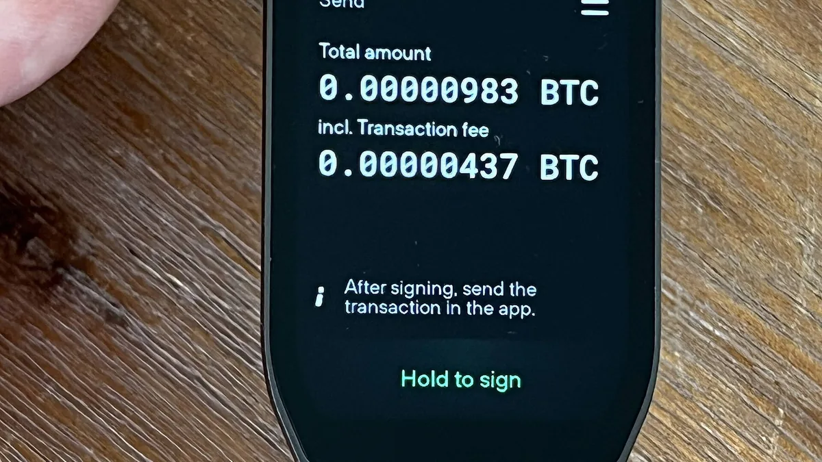 Trezor hardware wallet screen showing Bitcoin transaction details and a prompt to hold to sign.