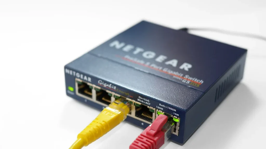 Netgear gigabit switch with yellow and red ethernet cables plugged into ports, on a white background.