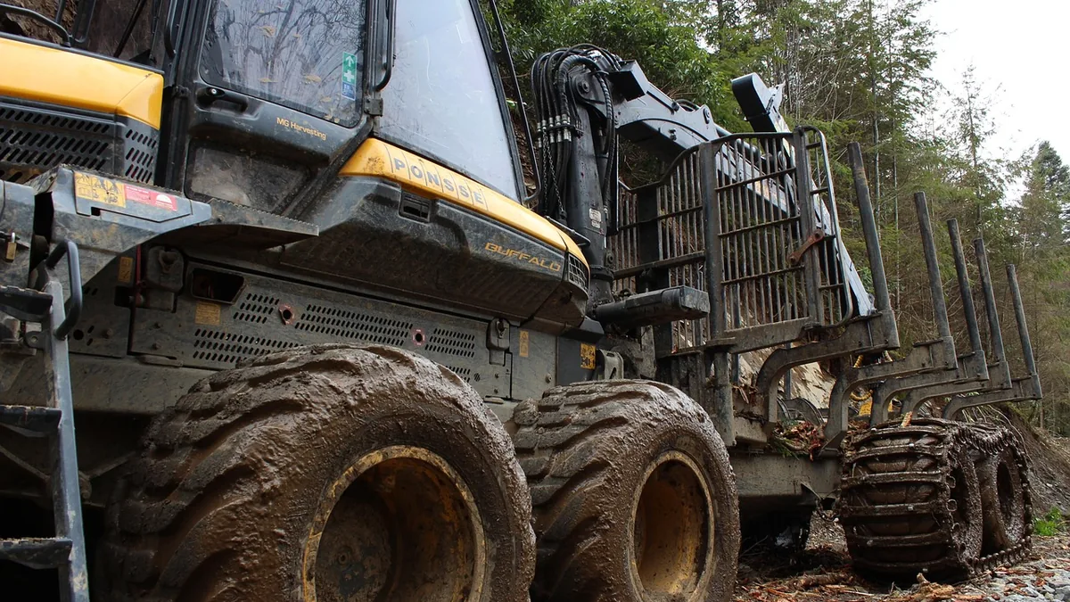 Muddy yellow Ponsse Buffalo forestry vehicle with large tires and tracks on a forest path.
