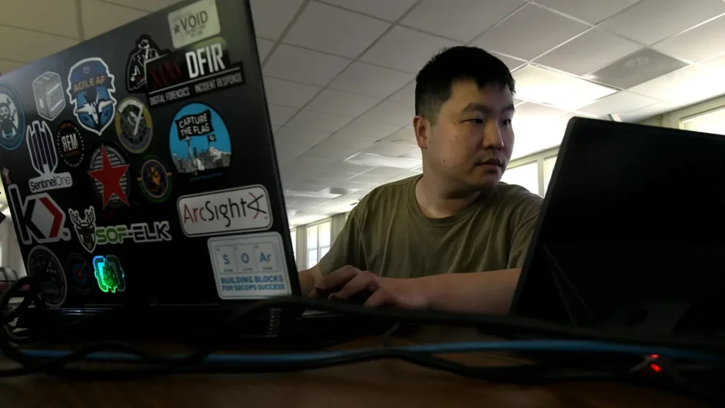 A cybersecurity analyst works at a laptop covered in security-related stickers.