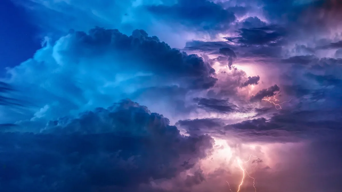 Vivid blue and purple storm clouds swirl around bright bolts of lightning in a dramatic sky.