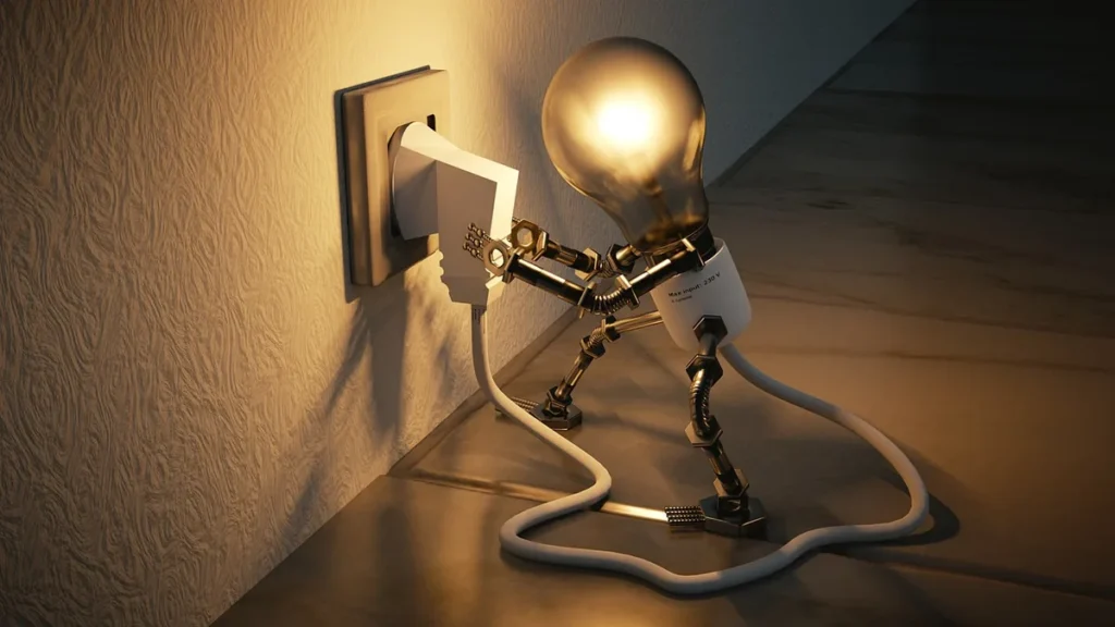 A lightbulb-headed robot figurine plugging a white cable into a wall socket under warm light.