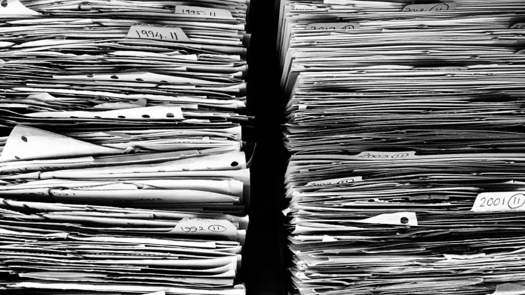 High-contrast black and white photo of massive stacks of paper files labeled with years, representing vast data archives.